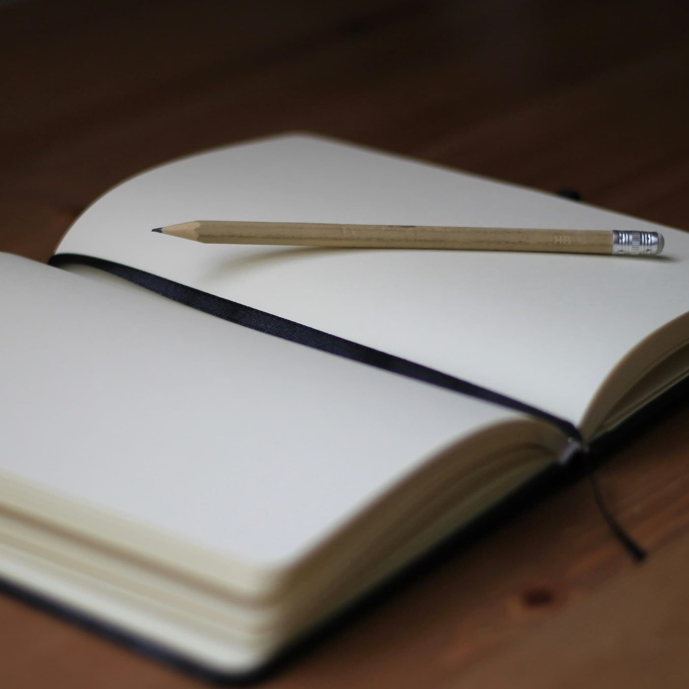 An open notebook with entirely blank pages and a sharpened pencil resting across it