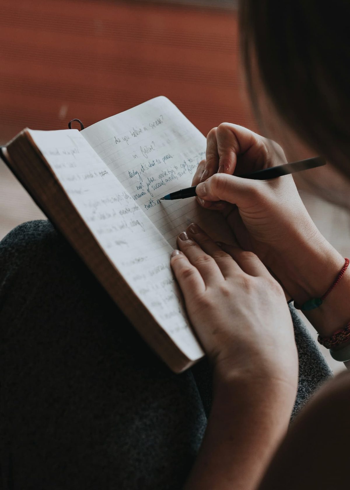 A woman sitting with a notebook on her lap, writing a page of handwritten reflections in pen
