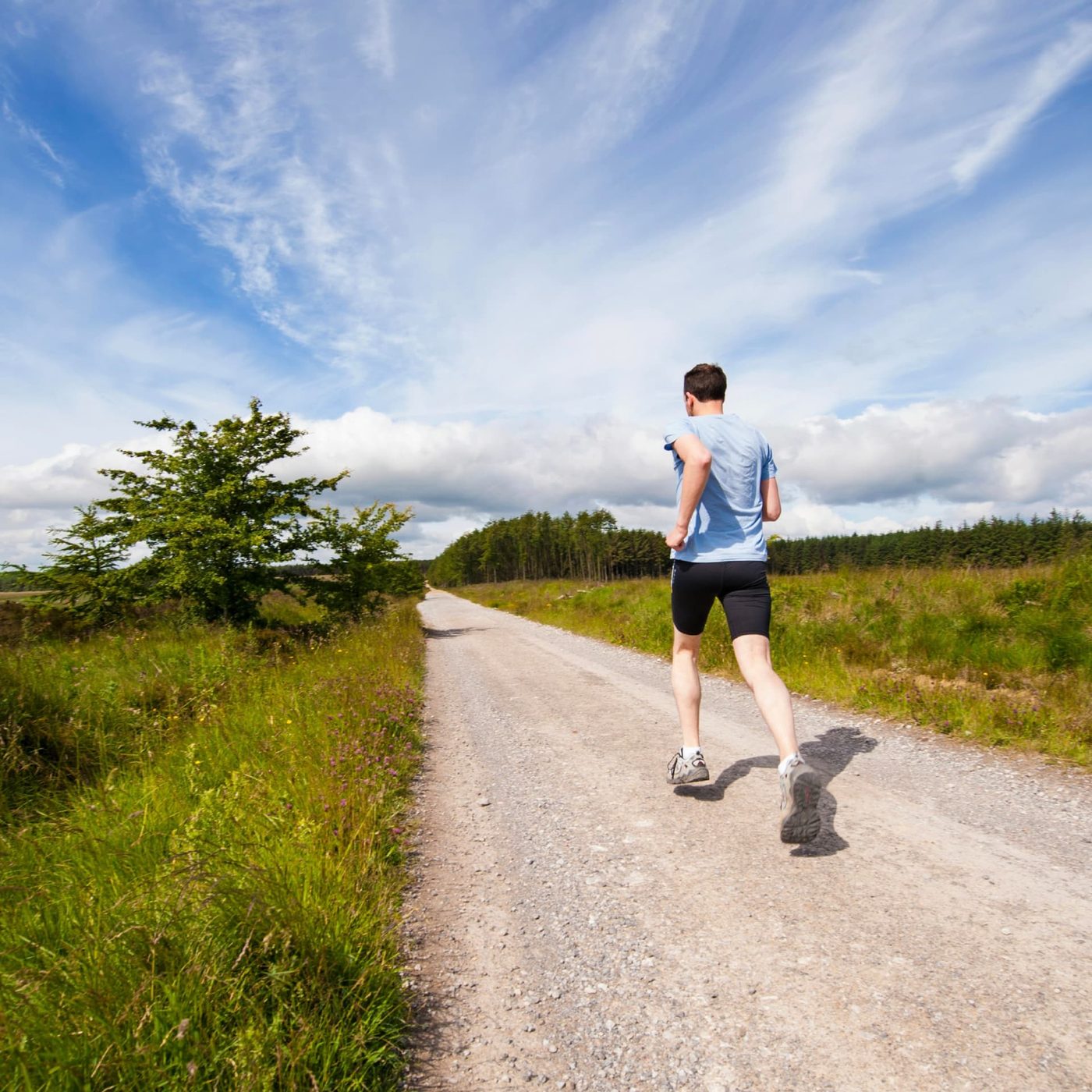A runner on a gravel track through open countryside under a blue sky with scattered cloud