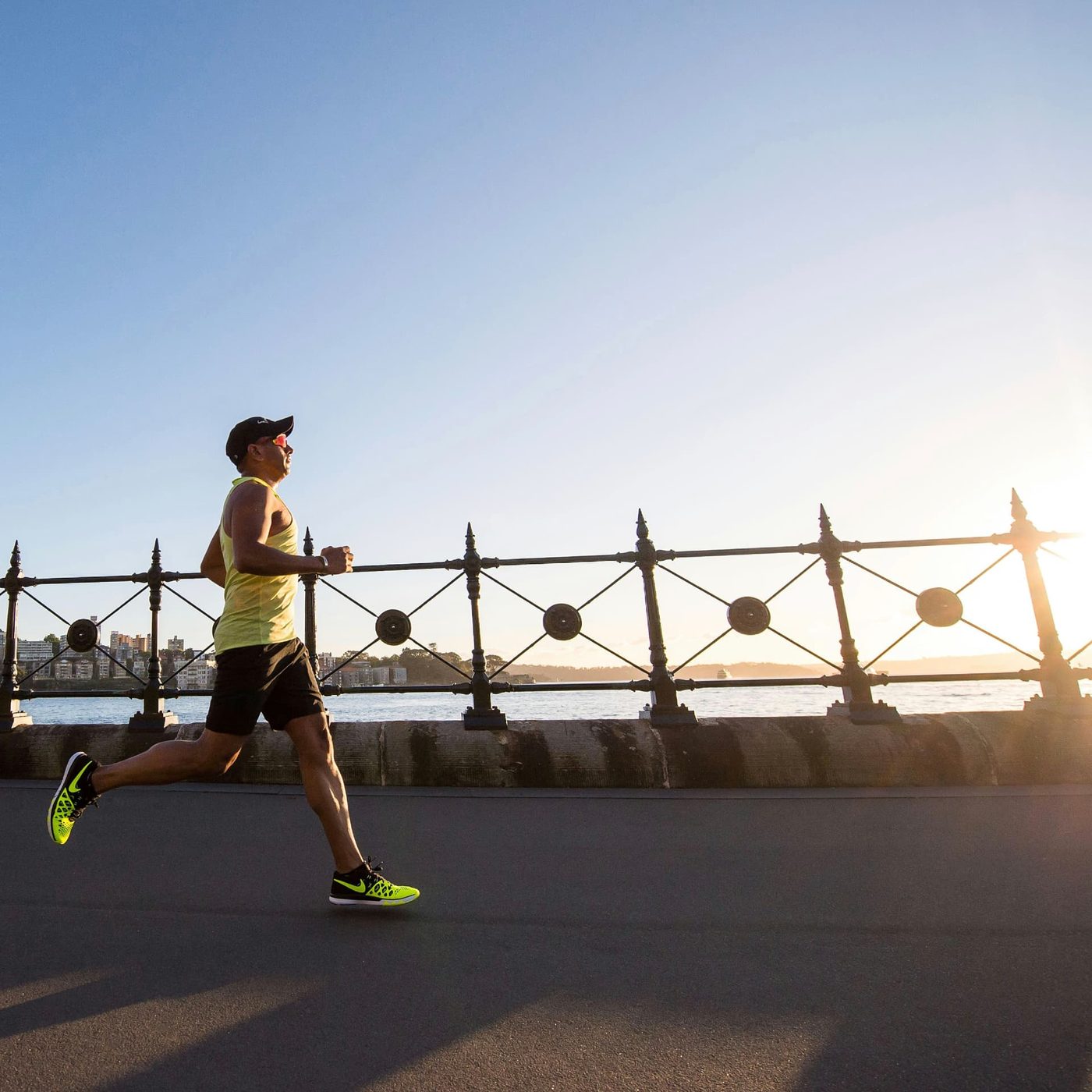 A runner in a bright vest running along a seafront promenade beside railings in low sunlight