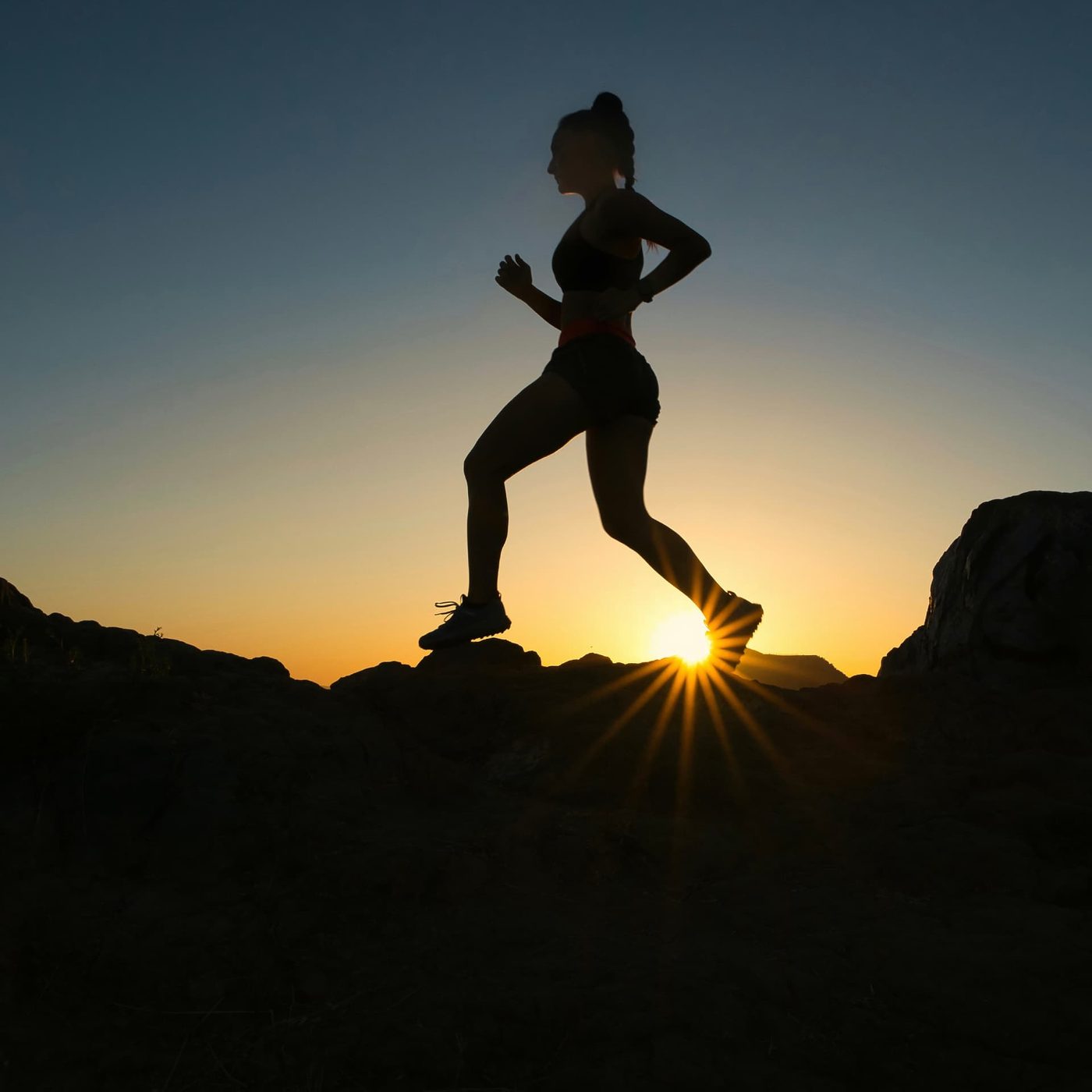 A runner silhouetted on rocks against a sunrise, one foot lifting from the ground